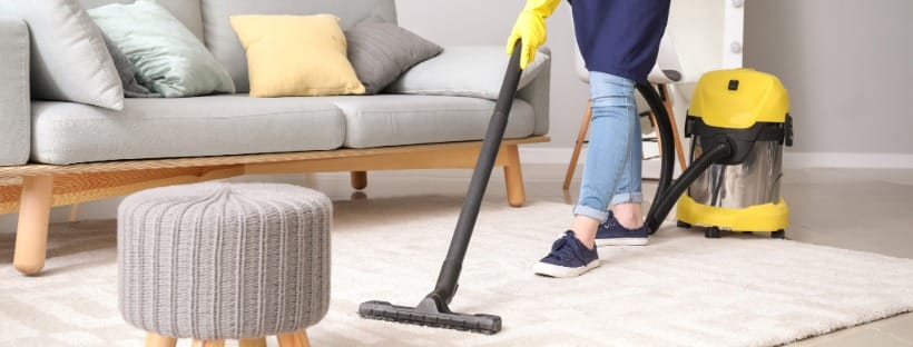A home-cleaning professional vacuums a carpeted living room, showcasing local service providers available through CB Preferred Providers.
