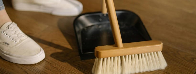 Person sweeping debris into a dustpan on a hardwood floor during a quick post-holiday clean up.