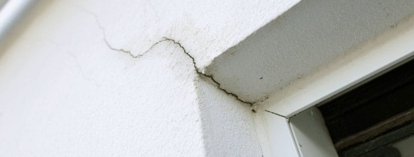 Close-up of a cracked exterior wall near a window frame highlighting potential structural issues found in a home inspection.